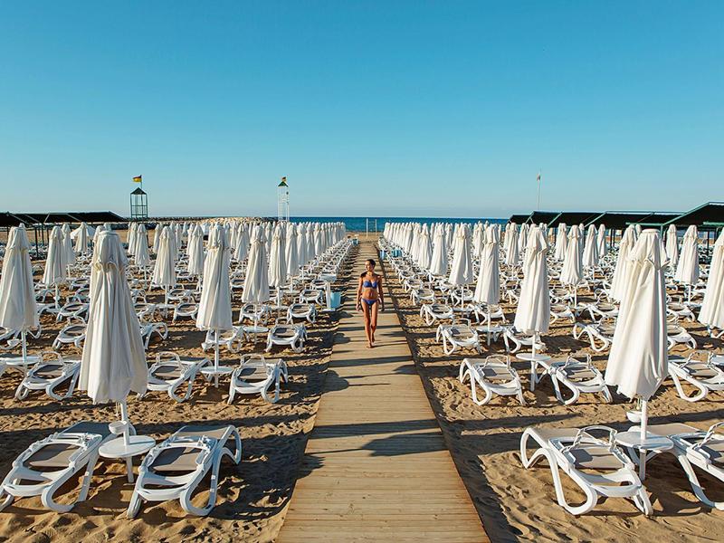 Strand met veel witte parasols en ligbedden, heldere blauwe lucht.