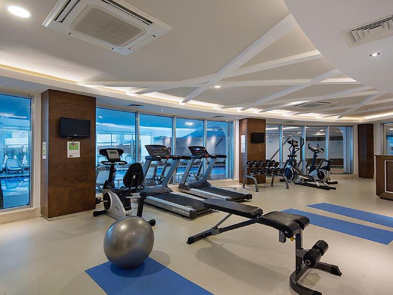 Moderne fitnessruimte met verschillende trainingsapparaten en grote ramen met uitzicht op de stad.