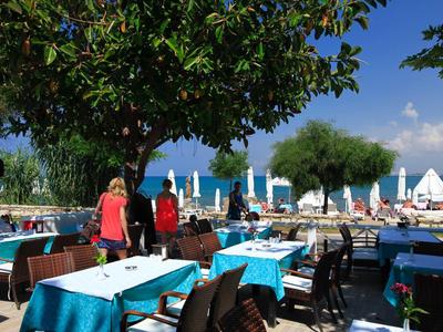 Venkovní část restaurace s modrými ubrusy, židlemi a bazénem pod modrou oblohou.