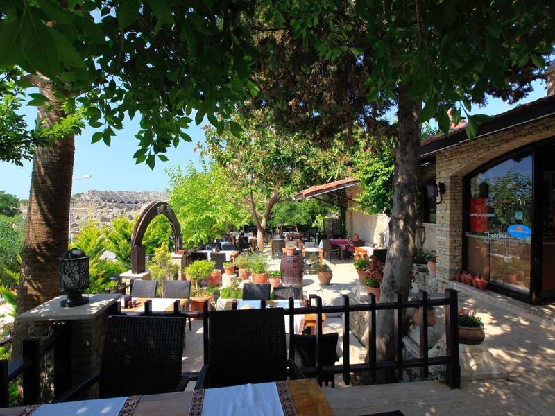 Slunná terasa s stromy, posezením a výhledem na údolí a hory.