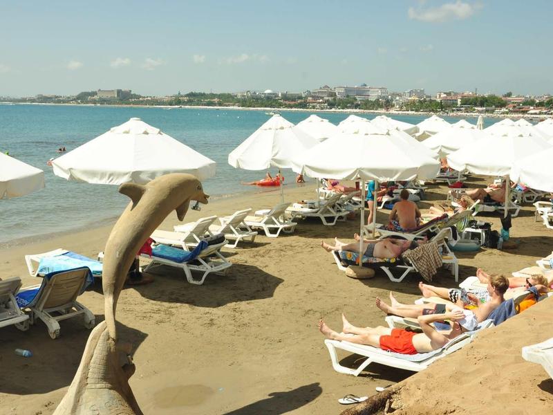 Pláž s lehátky a bílými slunečníky u moře za jasného počasí.