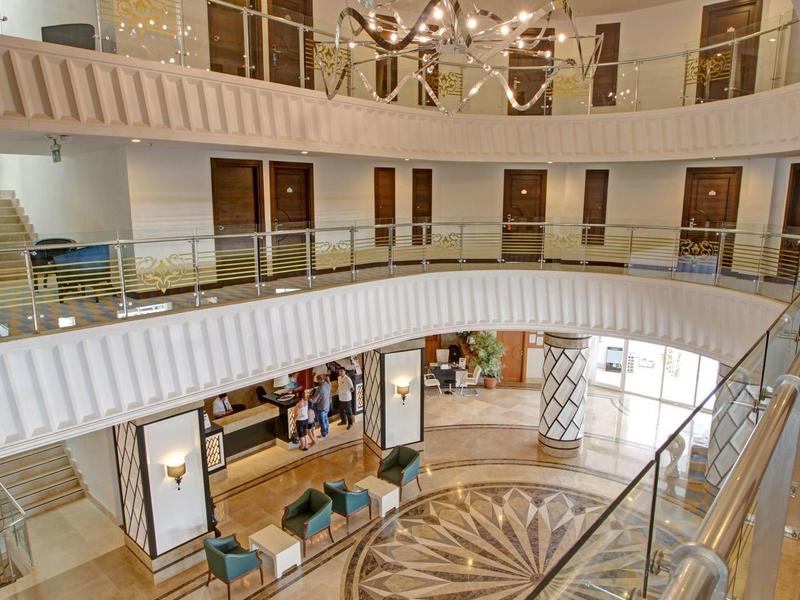 Lobby d'hôtel ouverte avec plusieurs étages, lustre et élégant motif de sol en marbre.