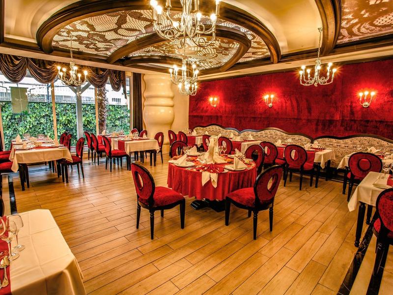 Restaurant élégant avec chaises rembourrées rouges, peinture artistique au plafond et lustres.