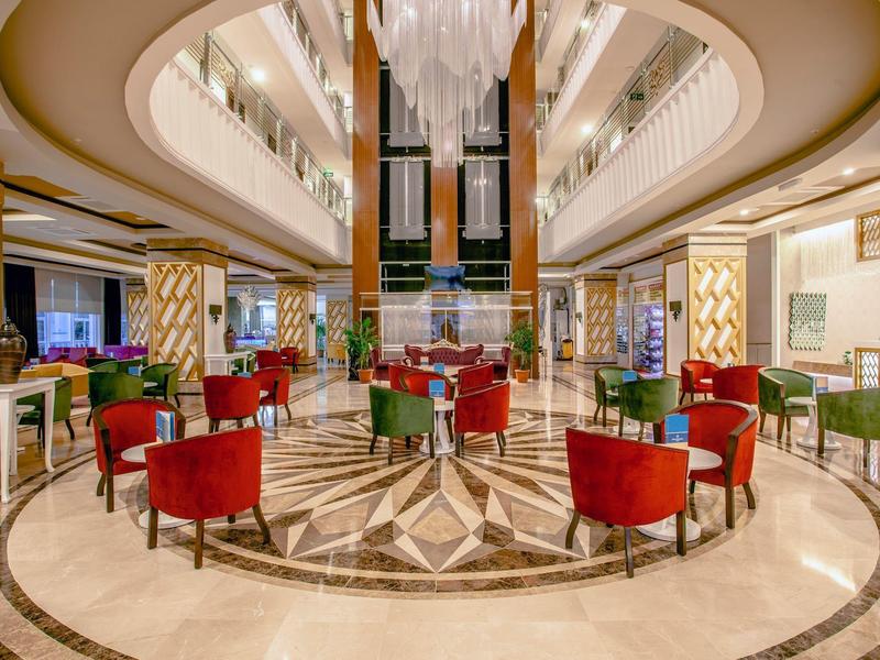 Lobby d'hôtel élégante avec des fauteuils rouges et un ascenseur en verre au centre.