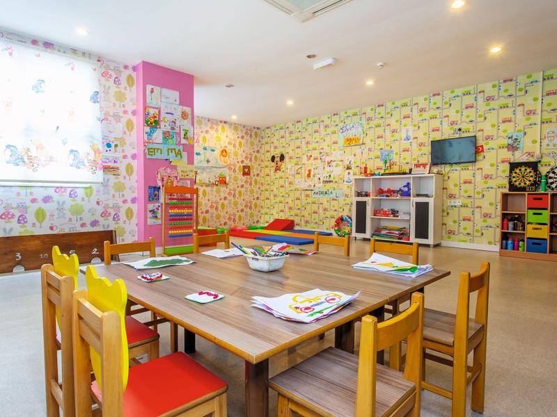 Salle de jeux et d'activités manuelles colorée pour enfants avec tables, chaises et jouets.