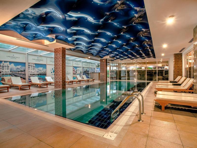 Piscine intérieure luxueuse avec plafond ondulé bleu et chaises longues confortables dans un hôtel.