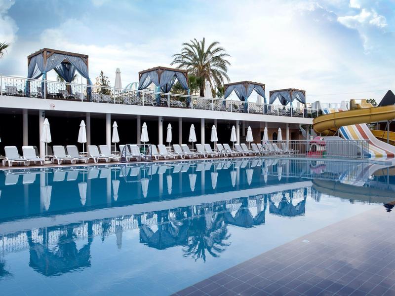 Grande piscine d'hôtel avec chaises longues, parasols, cascade et toboggans sous un ciel bleu.