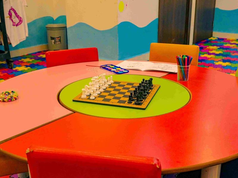 Table ronde colorée avec un échiquier et des crayons dans une salle adaptée aux enfants.