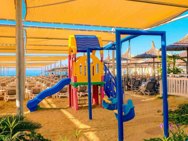 Aire de jeux colorée avec toboggan et structure d'escalade sous un auvent jaune près des chaises de plage.