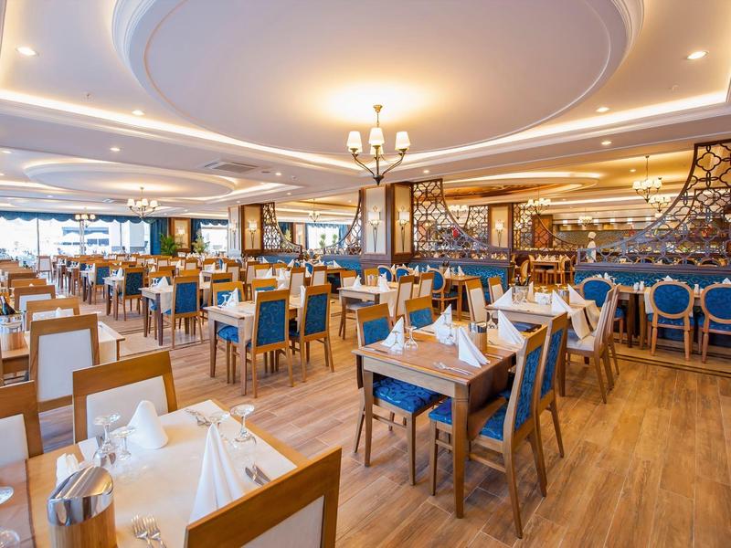 Grand restaurant d'hôtel lumineux avec sol en bois et tables élégamment dressées.