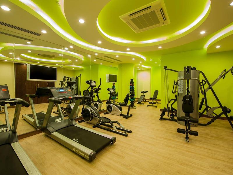 Salle de sport lumineuse avec équipements modernes et éclairage mural verdâtre.