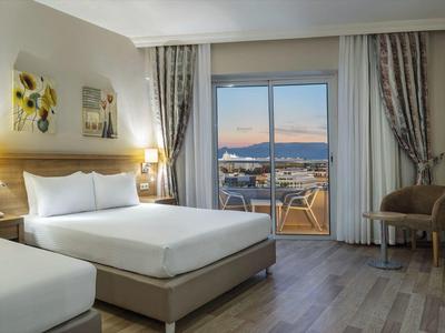 Camera d'hotel con letto matrimoniale e singolo, vista terrazza al tramonto.