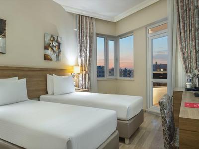 Camera d'hotel moderna con due letti, finestra con vista sul tramonto e scrivania con televisore.