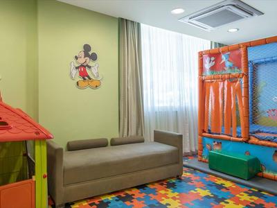 Angolo bambini con casetta, divano e piscina di palline colorate in una stanza luminosa.