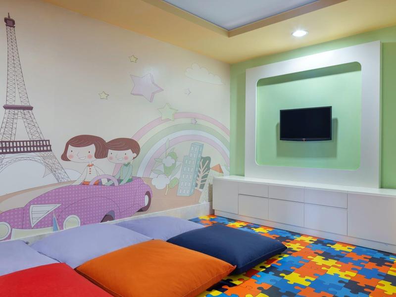 Angolo bambini colorato con cuscini, muro decorato con Torre Eiffel e bambini in auto.