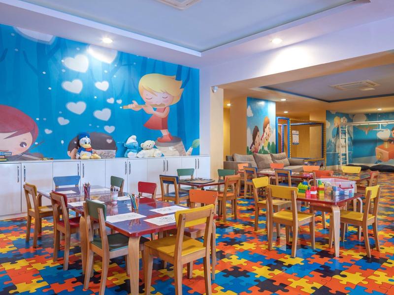 Sala da pranzo colorata con tavoli, sedie in legno e murale infantile.