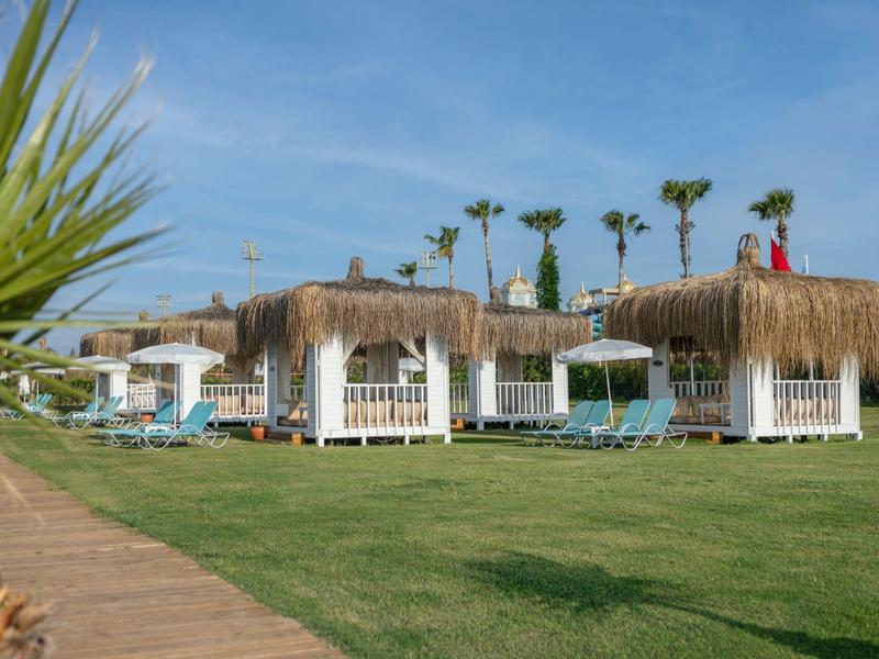 Gazebo in legno su prato verde con ombrelloni di paglia vicino al mare.