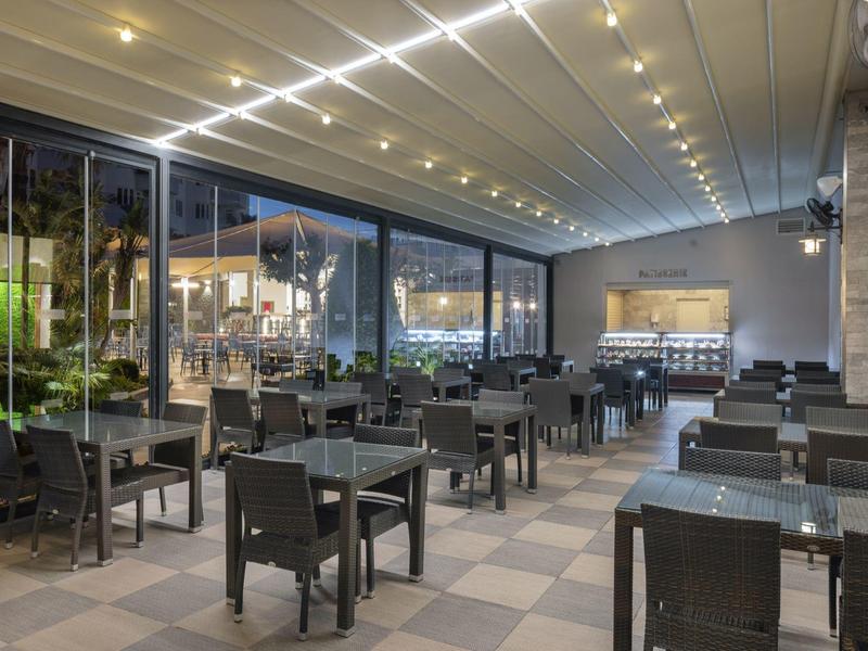 Terrazza di un ristorante moderno con tavoli in vetro e sedie in vimini, illuminazione accogliente.