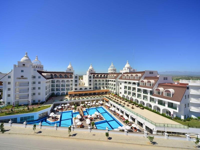 Large hotel with multiple pools and sun umbrellas under clear blue sky.