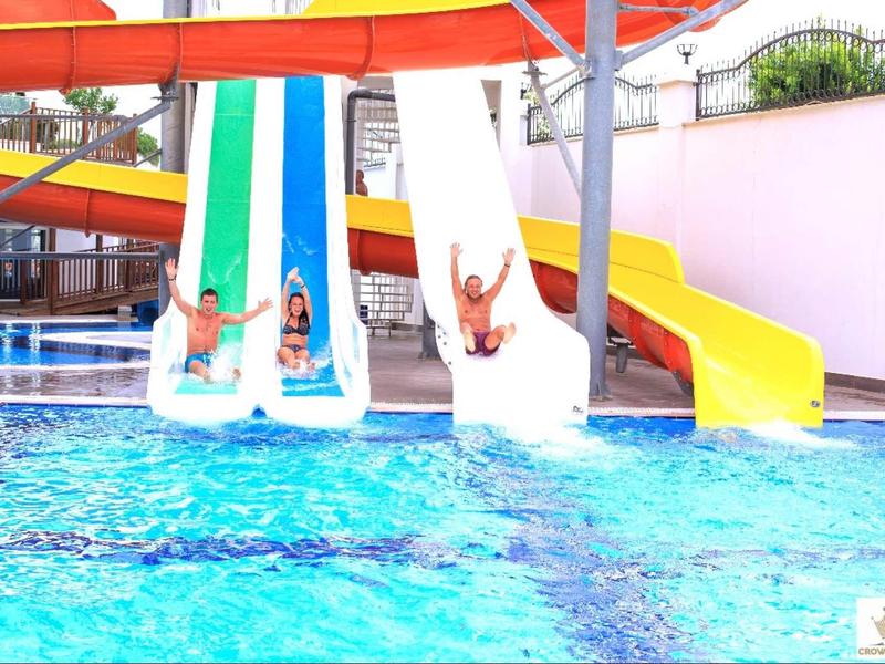 Three children sliding down colorful water slides into an outdoor swimming pool.