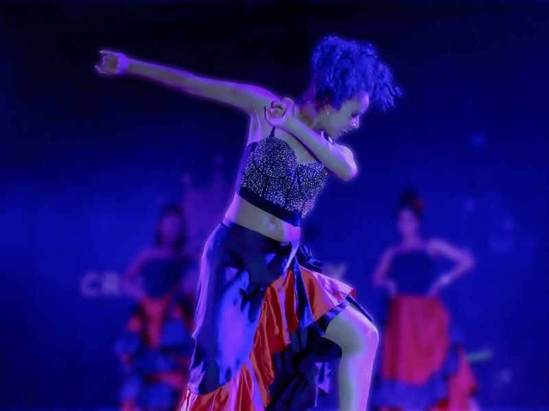 Woman in dance outfit performing on stage with blue and red lighting.