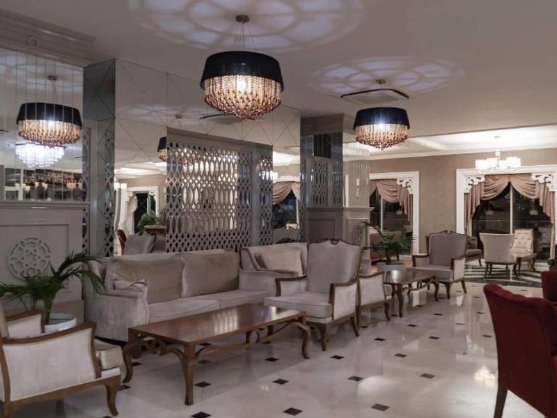 Elegant hotel lobby with armchairs, sofas, and chandeliers on marble flooring.