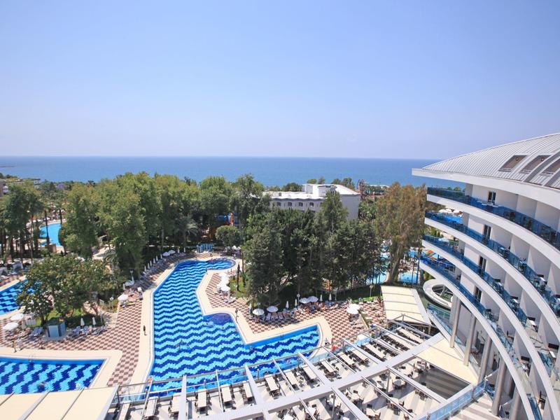 Velký hotelový bazén s lehátky a výhledem na moře za slunečného dne.