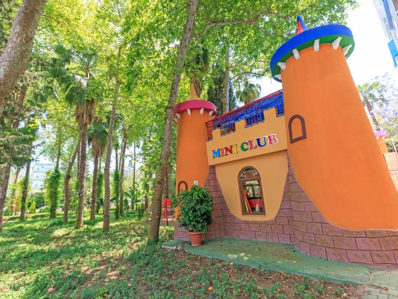 Barevné hřiště Mini Club v zahradě s stromy a zelení.