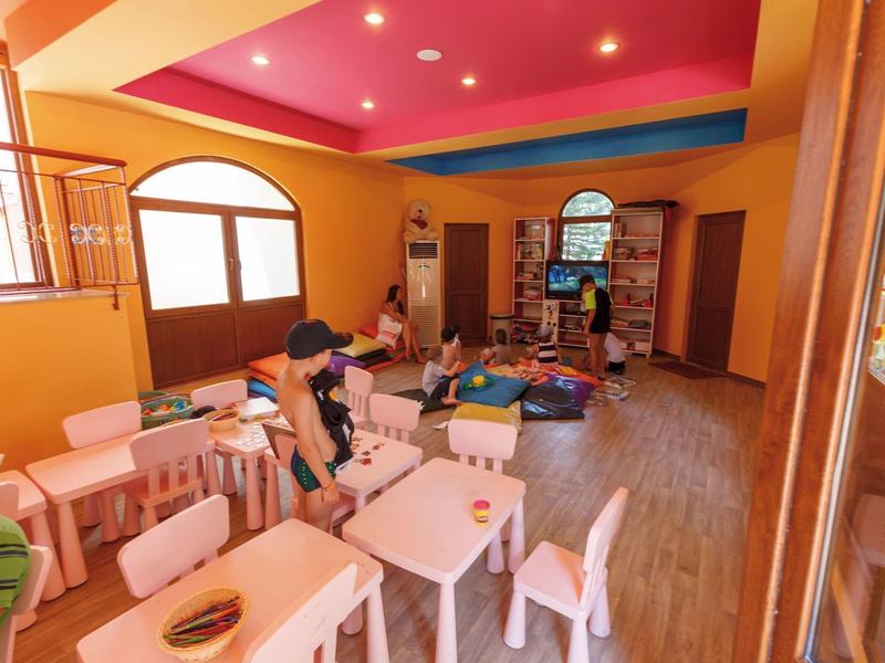 Barevná herna pro děti se stoly, dřevěnými hračkami a útulnou atmosférou.