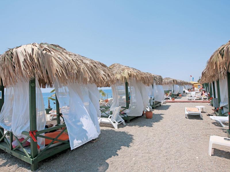 Pláž s lehátky a slaměnými slunečníky u moře pod jasnou oblohou.