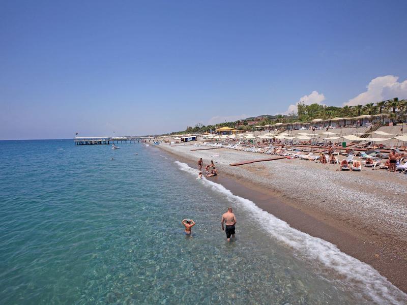 Pláž s čistou mořskou vodou, lehátky a slunečníky pod modrou oblohou.
