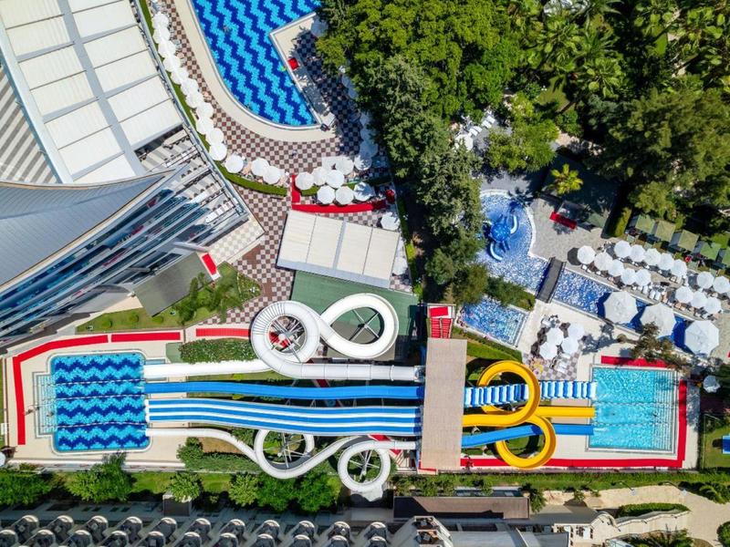 Letecký pohled na vodní park s bazény, tobogány a slunečníky v hotelovém resortu.