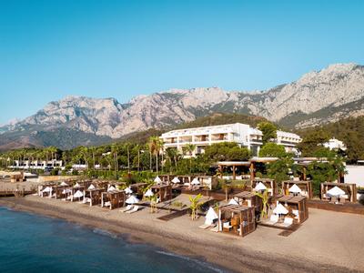 Hôtel de luxe avec lits de plage et montagnes en arrière-plan sous un ciel clair.