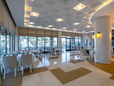 Salle de petit-déjeuner d'hôtel lumineuse et spacieuse avec tables et chaises blanches.
