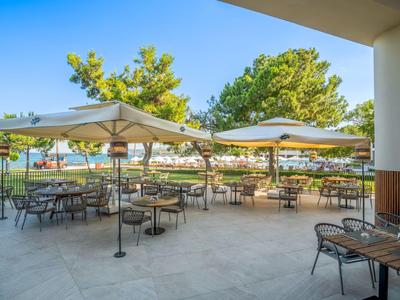 Terrasse avec tables et chaises sous de grands parasols, entourée d'arbres verts.