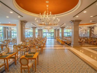 Salle à manger d'hôtel élégante avec lustre, tables et chaises sous une lumière chaude.