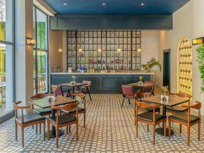 Espace bar d'hôtel moderne avec chaises en bois, sol à motifs et grandes fenêtres.