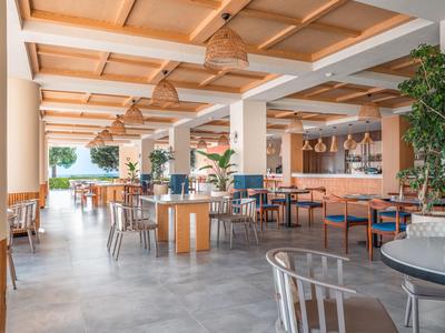 Restaurant d'hôtel lumineux et moderne avec mobilier en bois, plantes et grandes fenêtres donnant sur un lac.