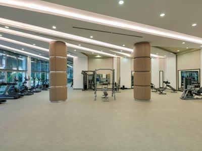 Salle de sport spacieuse avec équipements modernes et grandes fenêtres dans un hôtel lumineux.