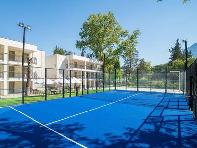 Surface de court de tennis bleue devant des bâtiments d'hôtel modernes avec des arbres et du soleil.