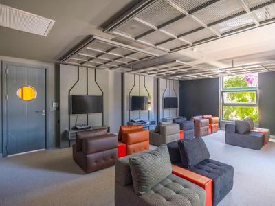 Salon d'hôtel moderne avec meubles rembourrés rouges et gris, grandes fenêtres et design minimaliste.