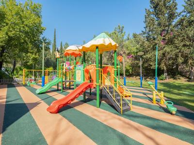 Aire de jeux colorée avec toboggans et structures d'escalade dans un parc boisé sous un ciel clair.