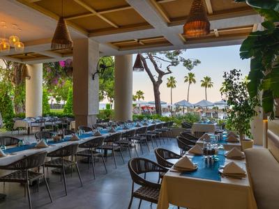 Terrasse d'hôtel couverte avec tables dressées et vue sur les palmiers et l'océan.