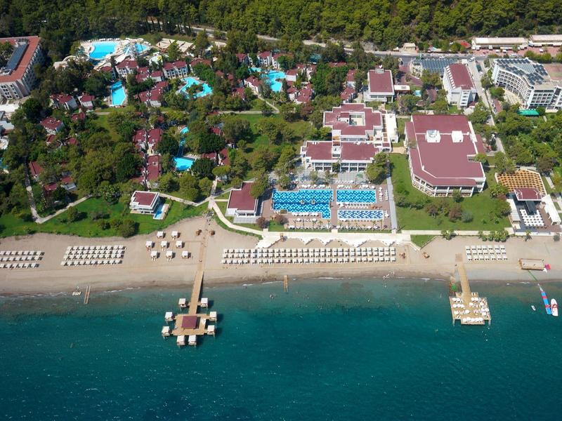 Vue aérienne d'un complexe hôtelier avec piscines, plage aménagée et forêt en arrière-plan.