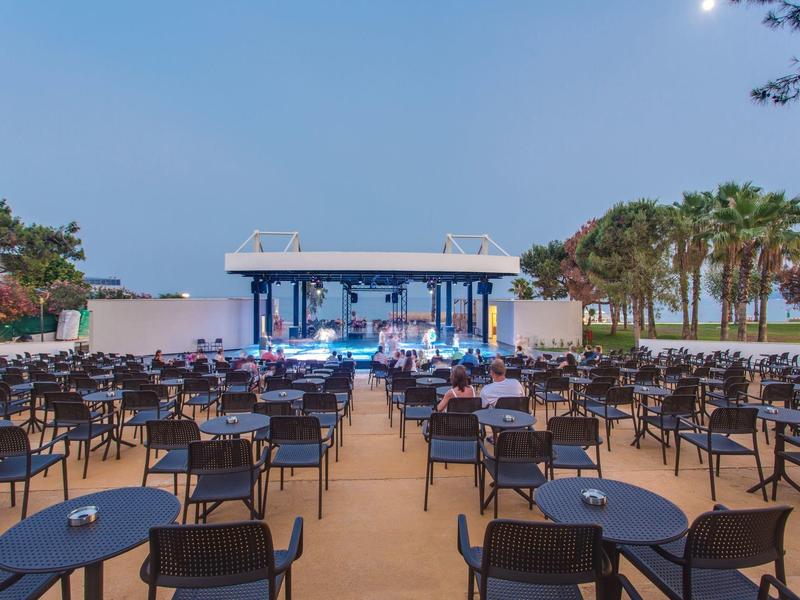 Grand espace extérieur avec tables, chaises et scène, décoré pour un événement en soirée.