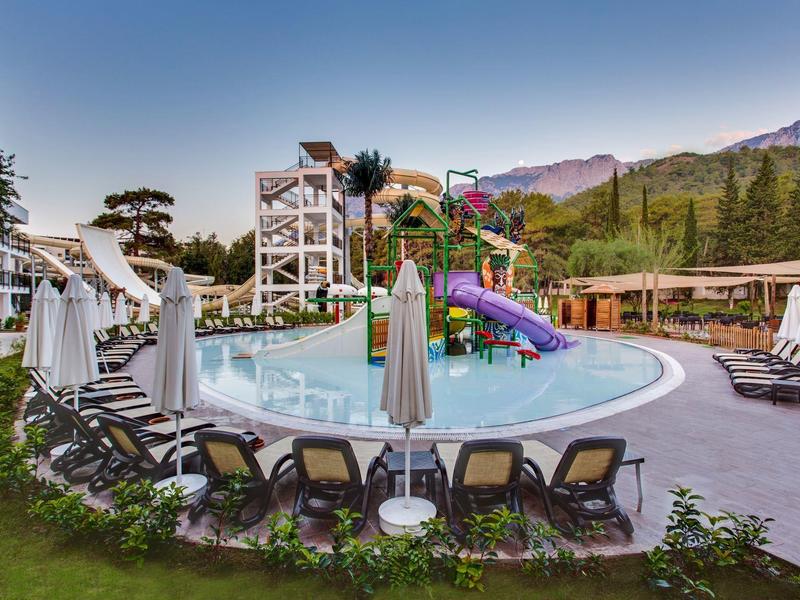 Piscine ronde avec toboggans colorés et chaises longues sous parasols blancs.