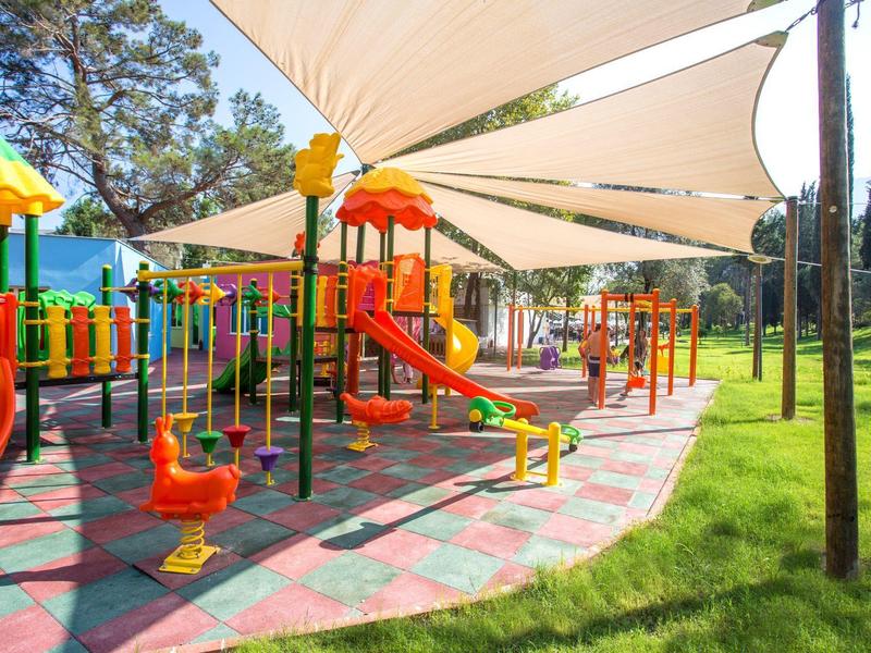 Aire de jeux colorée avec toboggans et balançoires sous un abri dans un parc verdoyant.