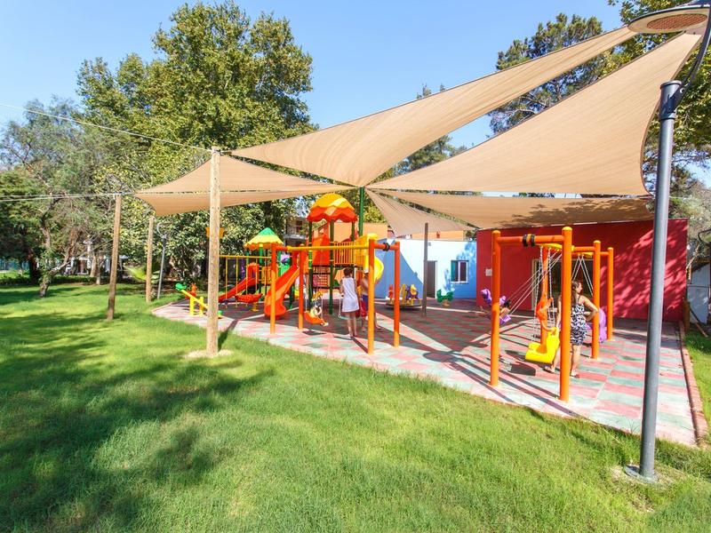 Terrain de jeux extérieur ombragé dans un parc verdoyant avec équipements colorés.