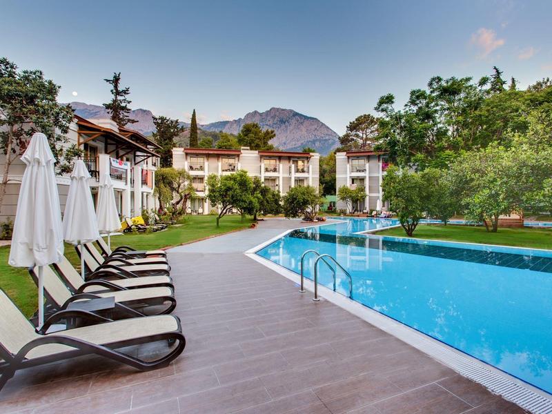 Piscine extérieure avec chaises longues et parasols, entourée de verdure et bâtiments.