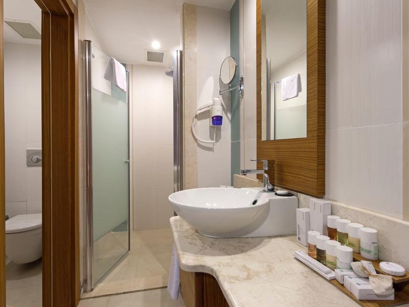 Salle de bain d'hôtel moderne avec vasque ronde, douche vitrée et rangements en bois.